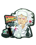 Picture of Dab To The Future dab pad next to a black lighter to show dab pad size. The top of the dab pad shows the phrase "Dab To The Future" in a Back To The Future font and style, on the left side of the pad. The majority of the pad is an animated picture of Doc Brown, with blood shot eyes, preparing to do a dab hit using an electronic dab rig, which is on the lower left part of the pad.